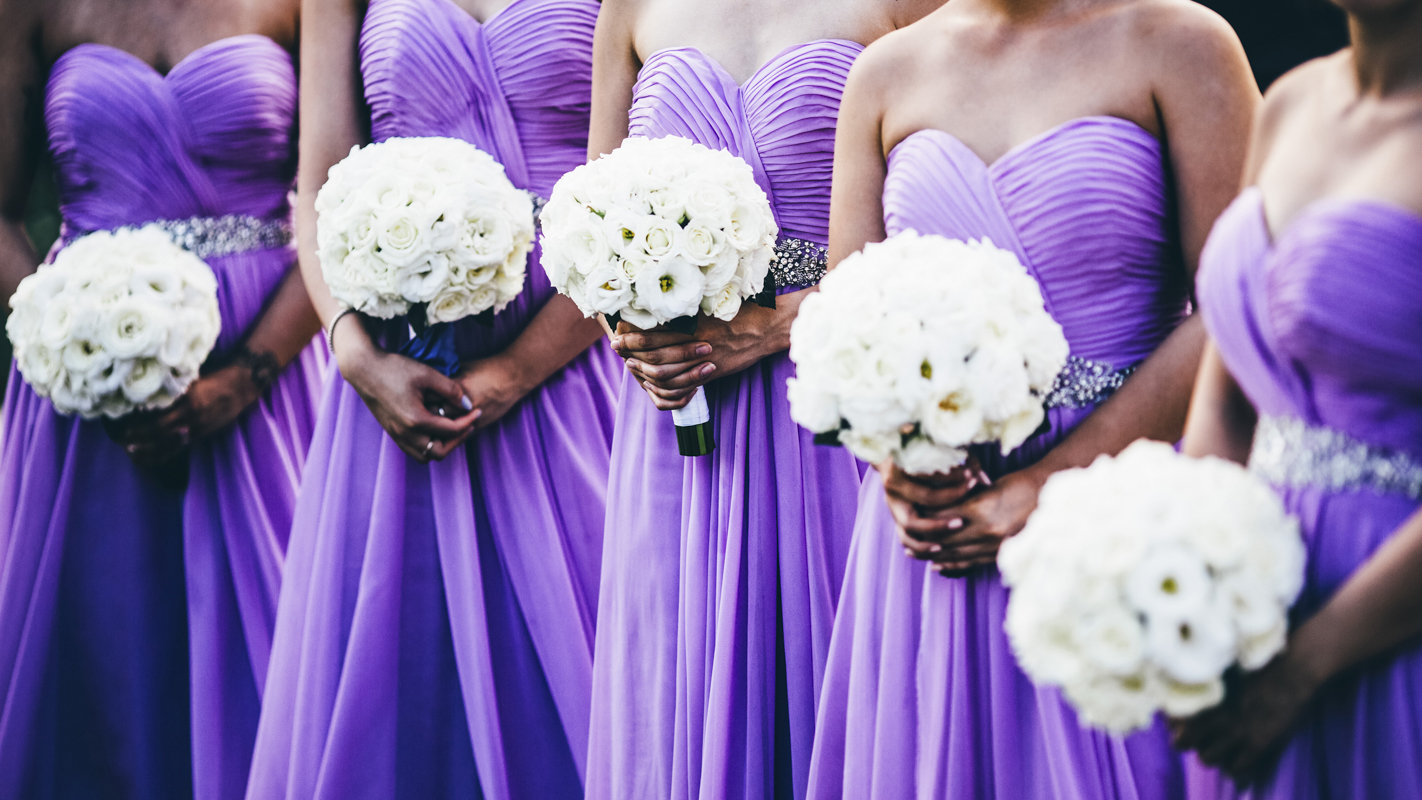 Wedding ceremony with bridesmaids wearing purple dresses and holding white flowers.