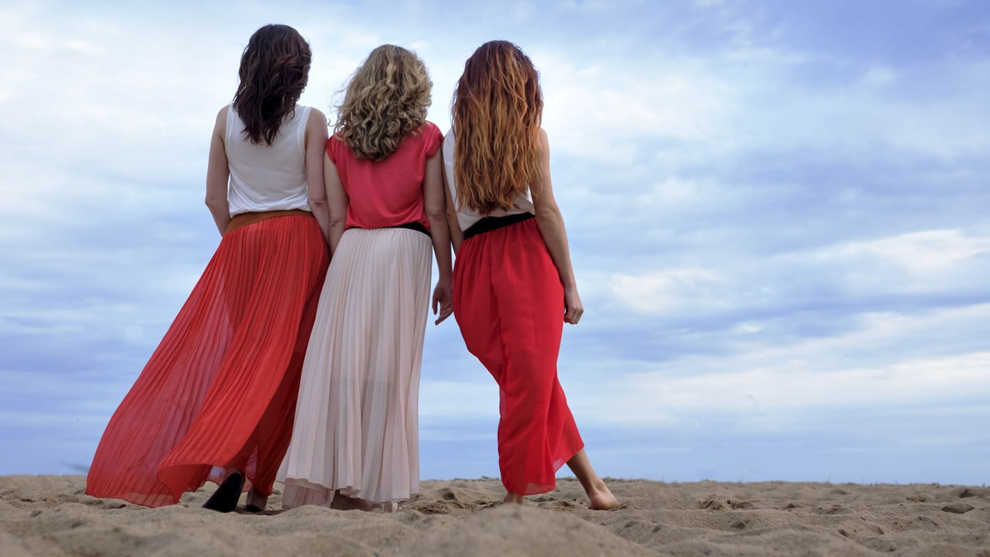Young women in a long dress standing on the beach in summer evening.